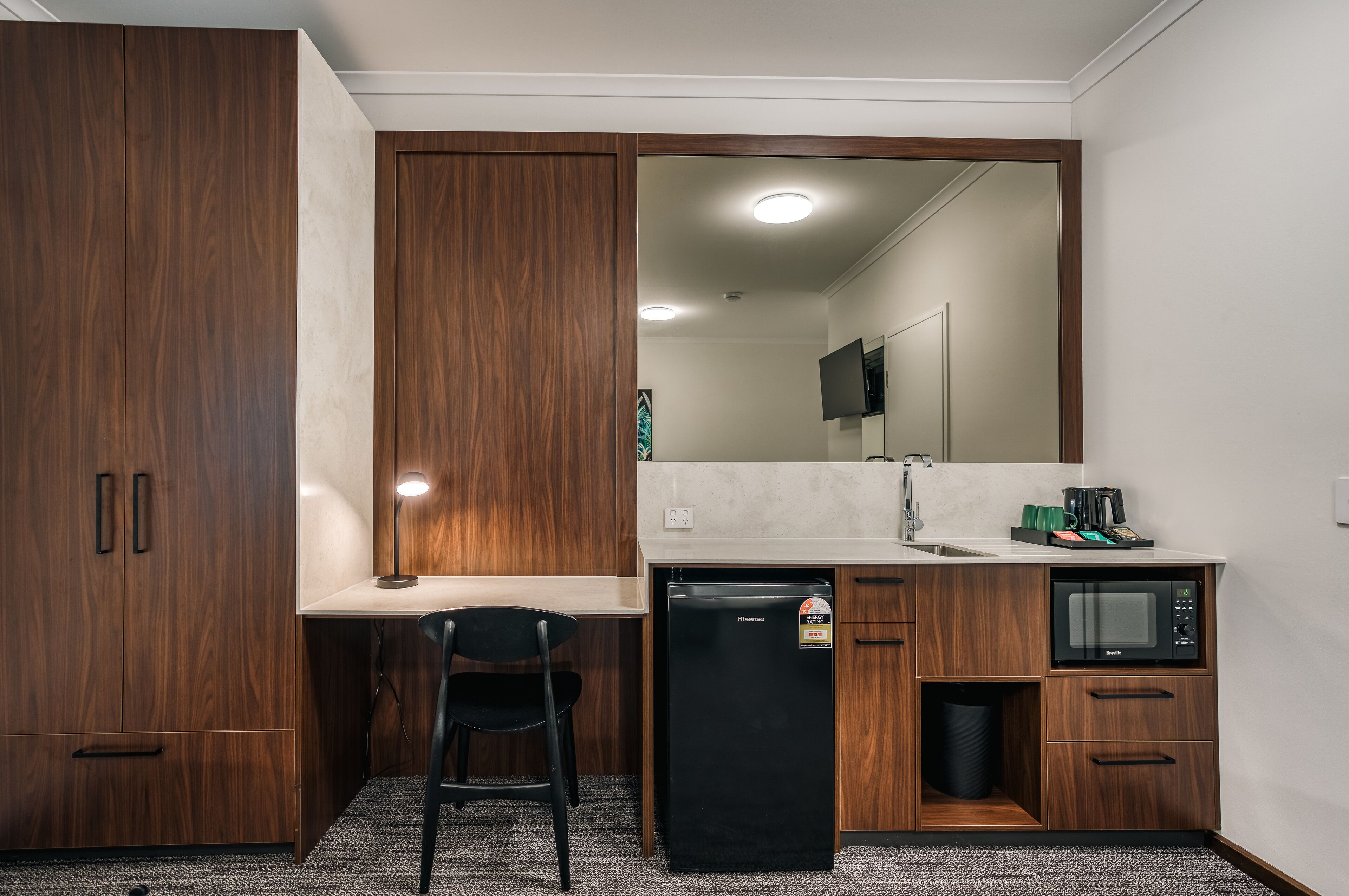 Una kitchenette compacta con refrigerador, microondas y lavamanos.