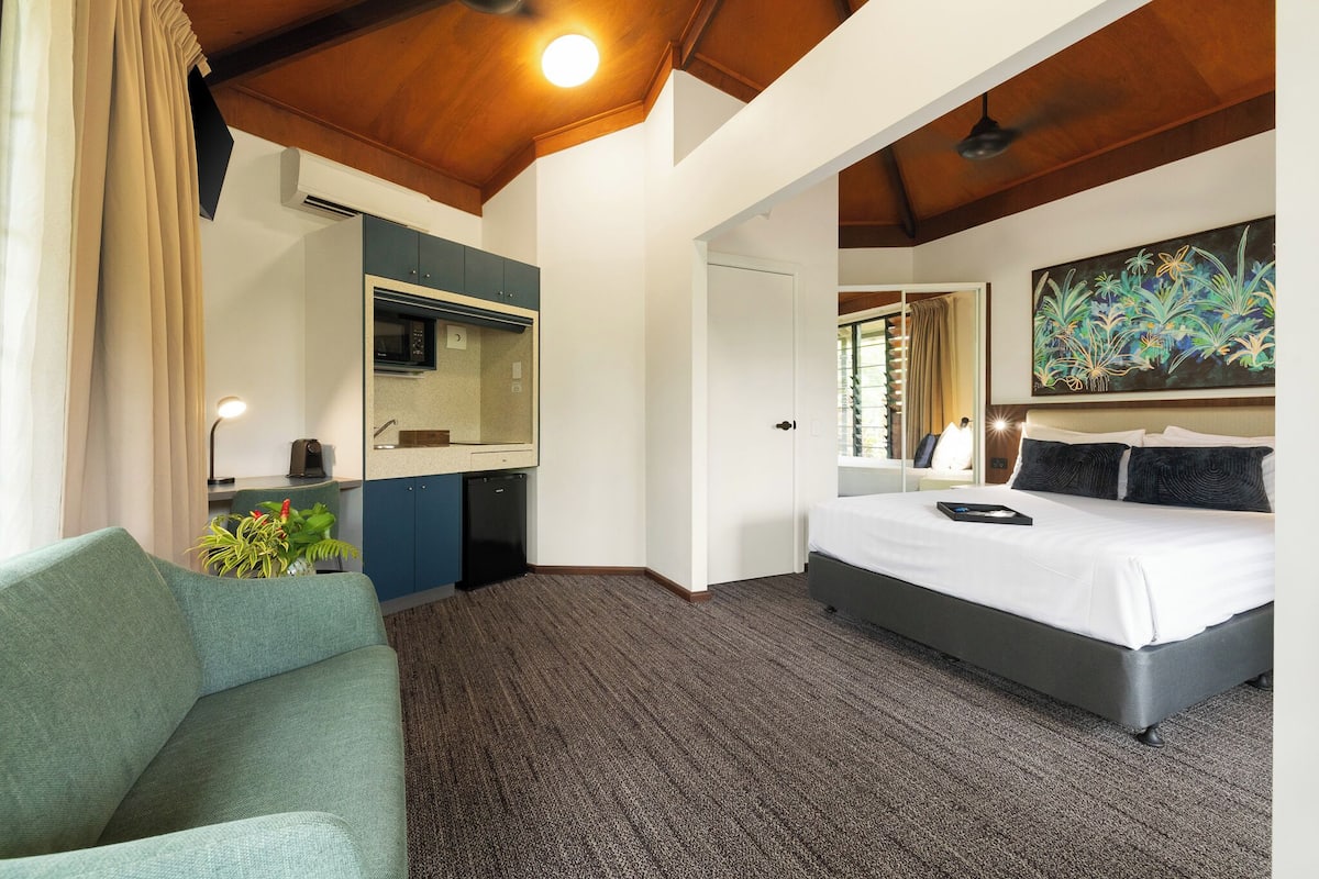 Habitación de hotel con cama, sofá, escritorio con computadora, microondas y un cuadro en la pared.