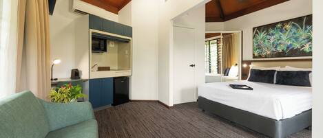 A hotel room with a bed, a sofa, a desk with a computer, a microwave, and a painting on the wall.