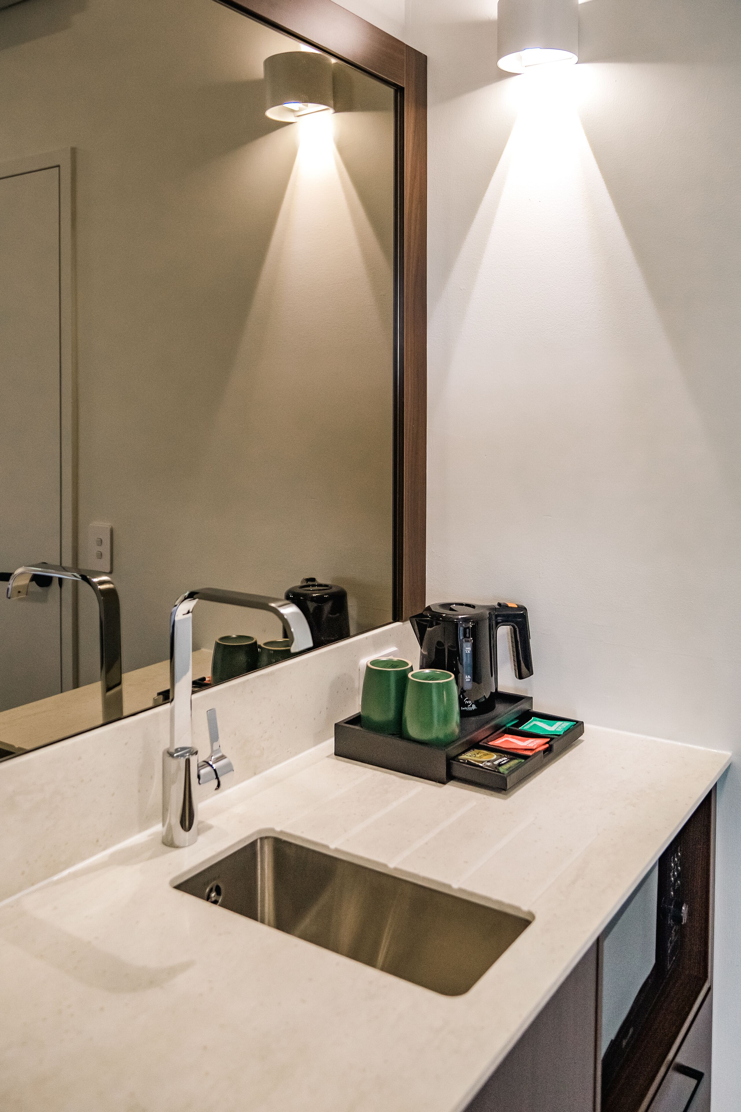 A modern bathroom with a sink, mirror, and coffee maker.