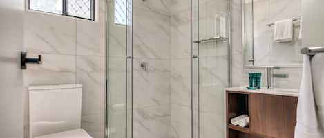 A modern bathroom with a glass-enclosed shower, a toilet, and a wooden vanity with a mirror.