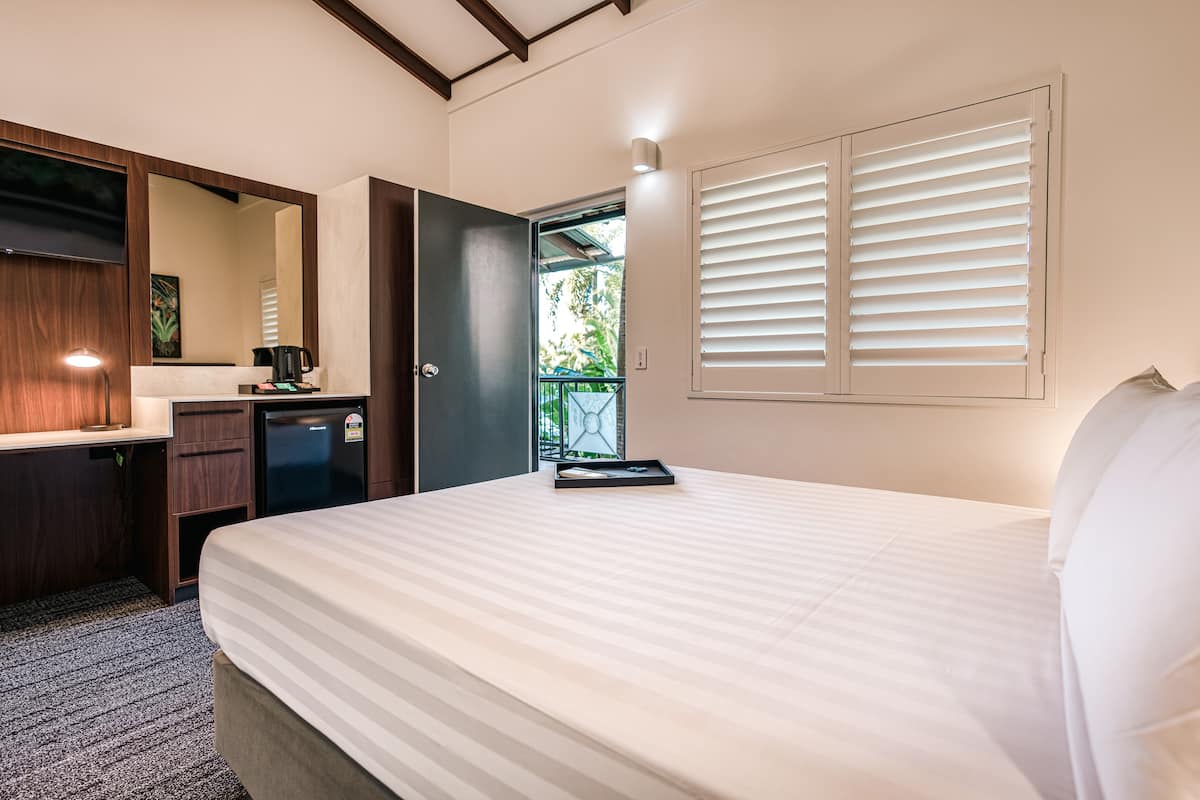 Habitación de hotel con cama, escritorio, espejo, refrigerador y ventana con persianas.