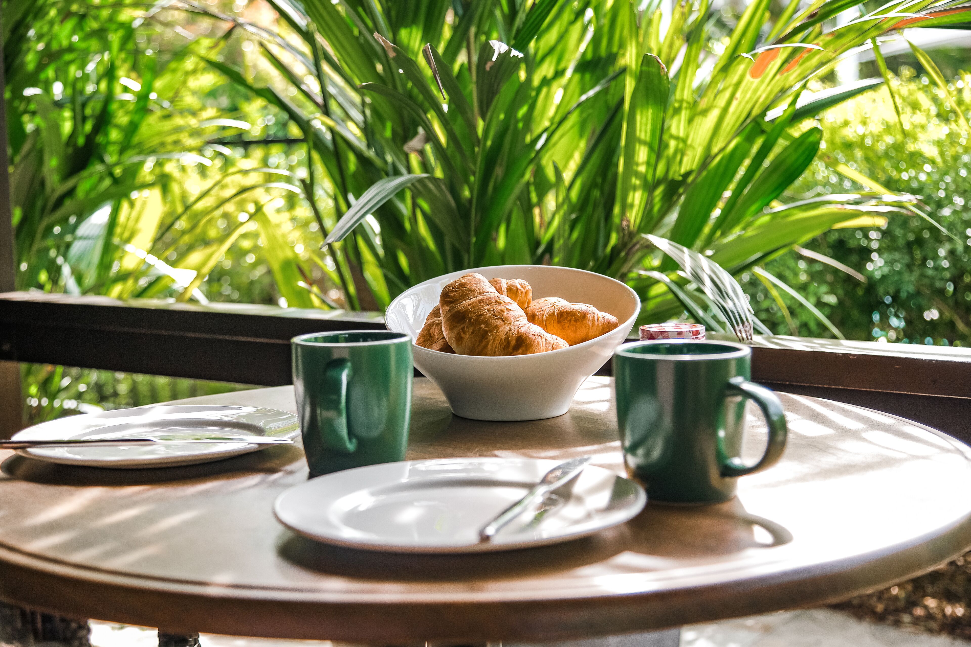 Una mesa de desayuno con cruasanes, un bol y dos tazas verdes.