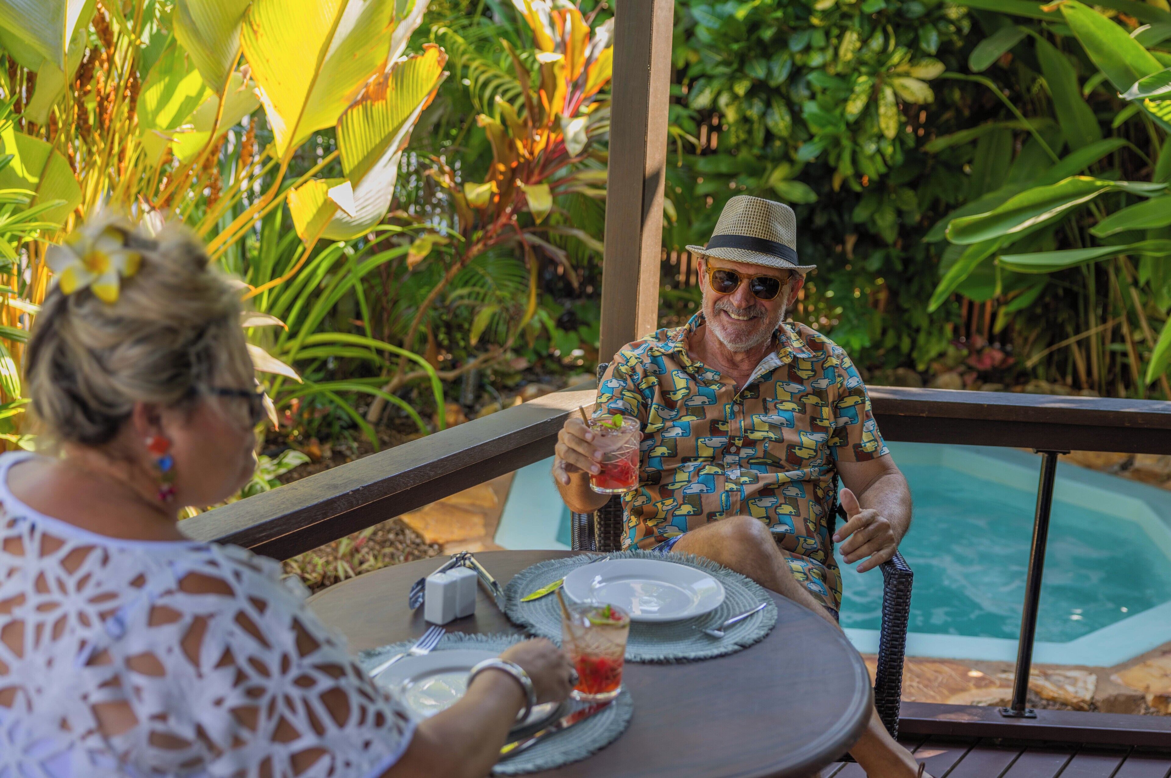 A man and a woman sitting at an outdoor table with a pool in the background.