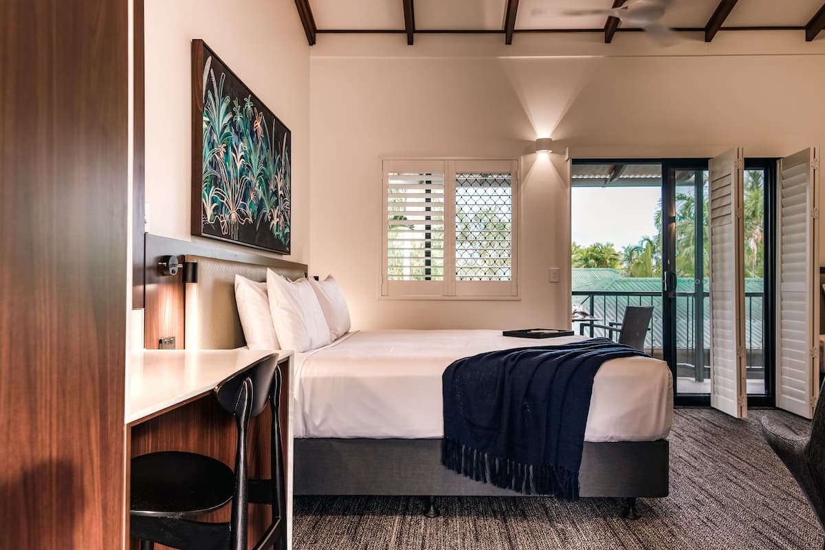 Un dormitorio con cama, escritorio y silla. Hay una ventana con persianas y vistas al exterior.