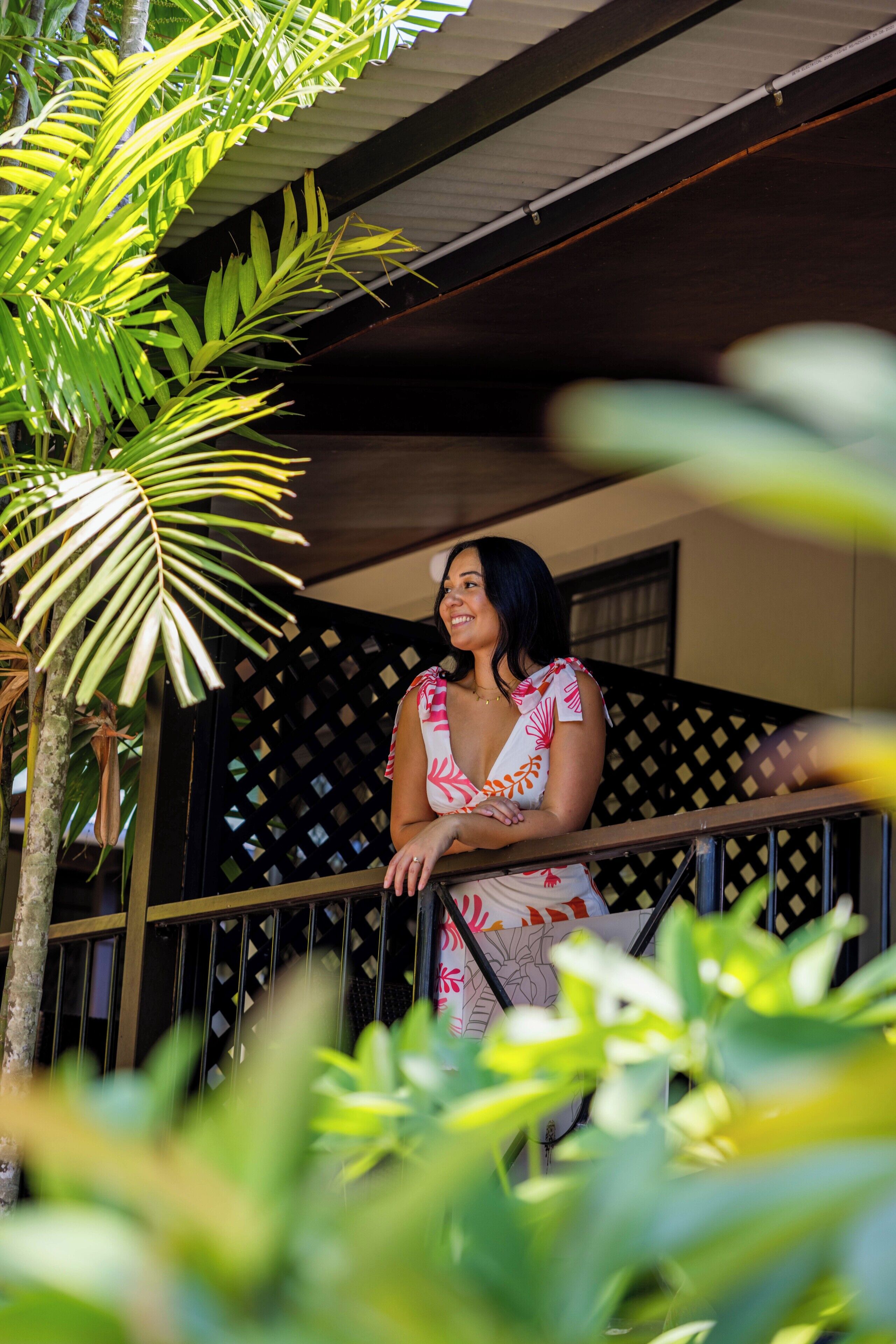 A person sitting on a balcony with a lattice wall and a palm tree in the foreground.