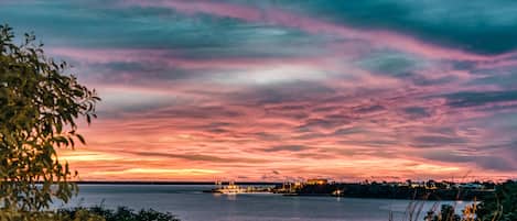 A waterfront view with a sunset and a distant illuminated structure.