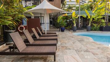 Uma área à beira da piscina com espreguiçadeiras, um espaço de estar coberto e uma piscina.