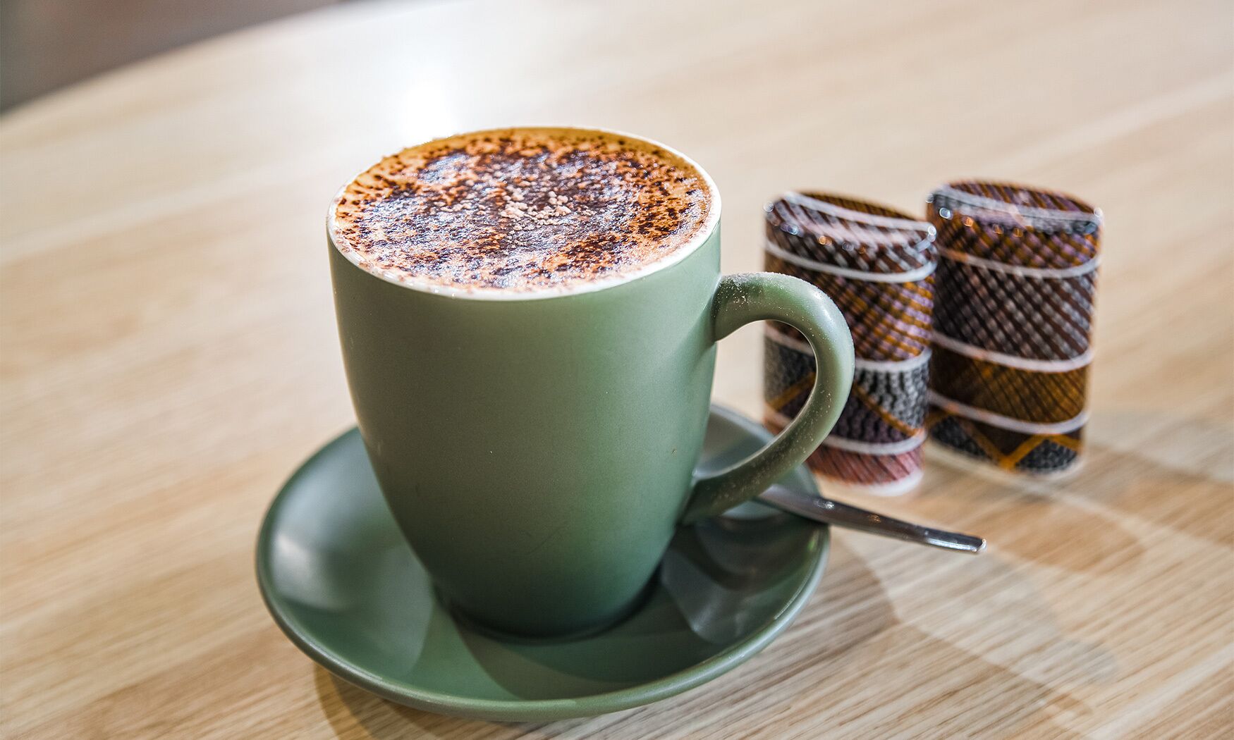 A cup of coffee with a frothy top on a saucer, placed on a wooden table.