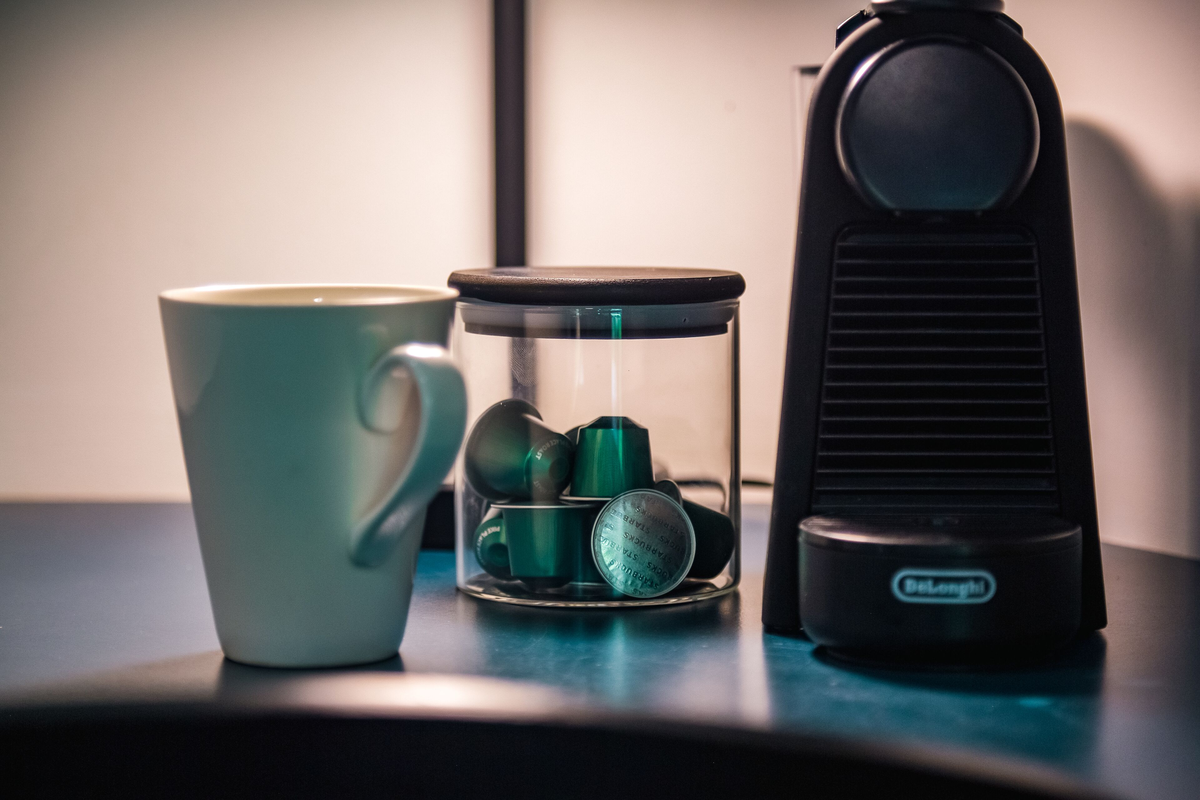 A coffee cup, a glass jar with green objects, and a black device on a table.