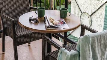 Una mesa redonda con sillas de mimbre, una revista y dos tazas verdes.