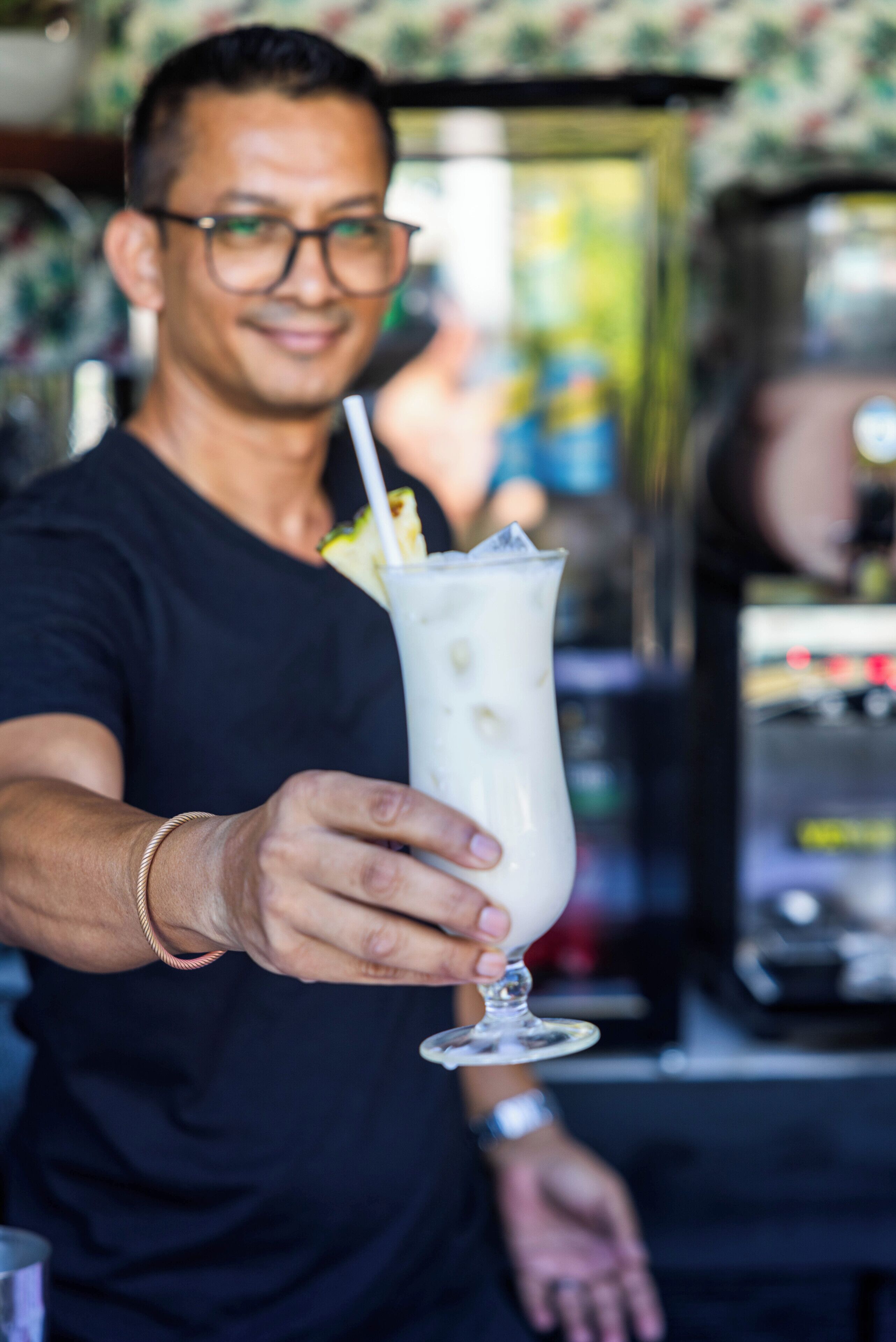 Une personne tenant un verre de lait frappé avec une paille, portant un t-shirt noir et un bracelet.