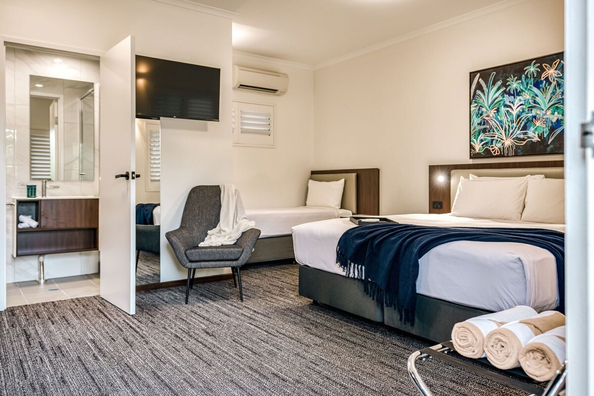 Une chambre d’hôtel avec un lit, une chaise, une télévision, un climatiseur et un tableau au mur.