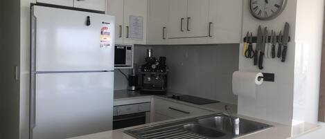 Una cocina moderna con armarios blancos, un refrigerador de acero inoxidable, un microondas, una máquina de espresso y un lavabo.
