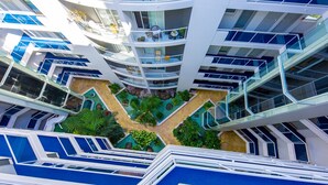 A multi-level hotel with interconnected balconies, a central courtyard with plants, and a modern architectural design. - Atrium Resort (Biggera Waters)