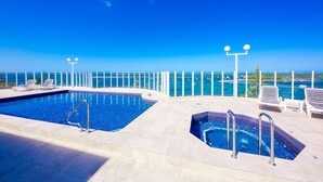 A rooftop pool with two hot tubs, lounge chairs, and a clear view of the ocean. - Atrium Resort (Biggera Waters)