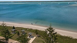A beach view with clear water, a sandy shore, and several small buildings with roofs. - Atrium Resort (Biggera Waters)