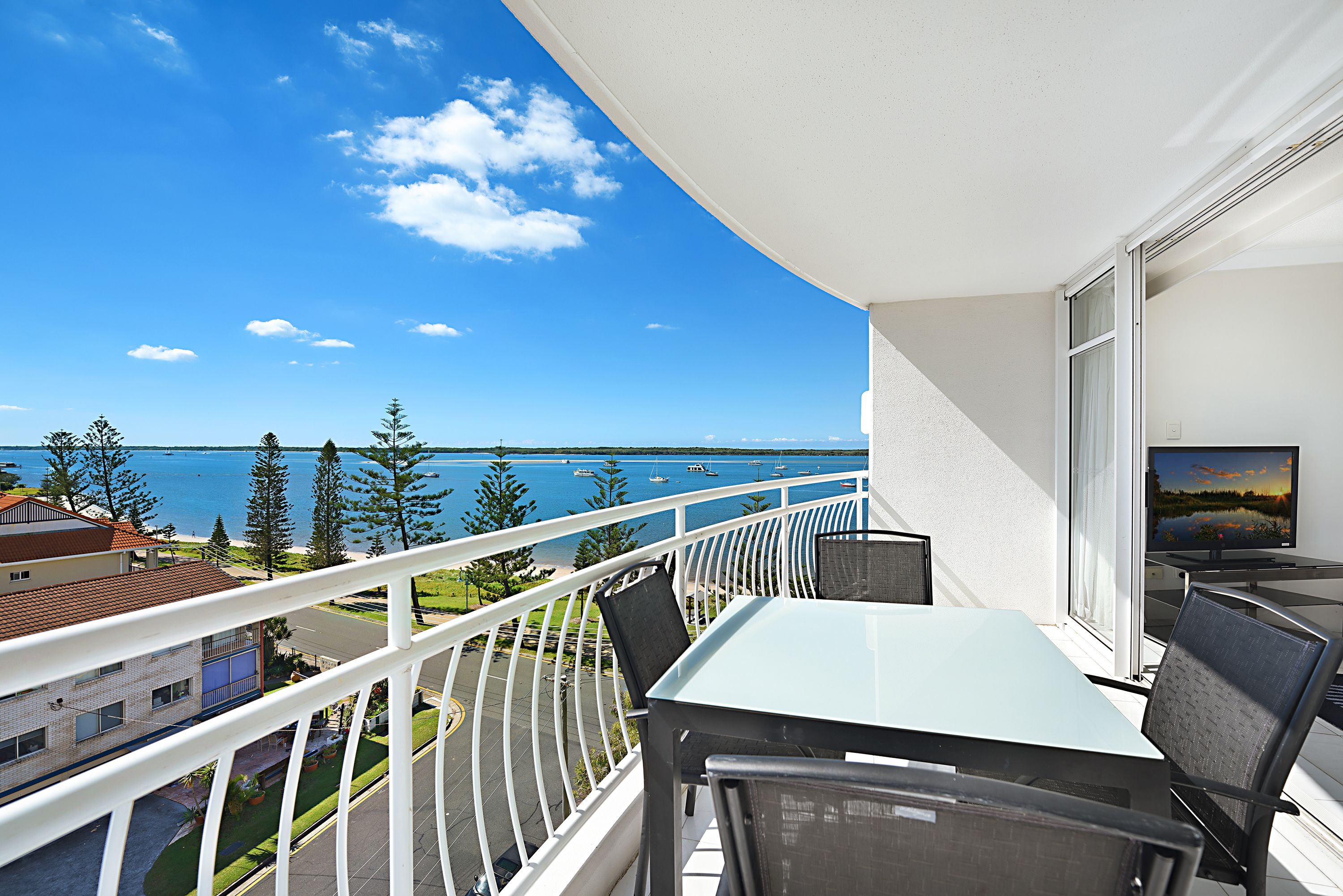 Un balcone con tavolo e sedie in vetro, vista su un corpo d'acqua e edifici.