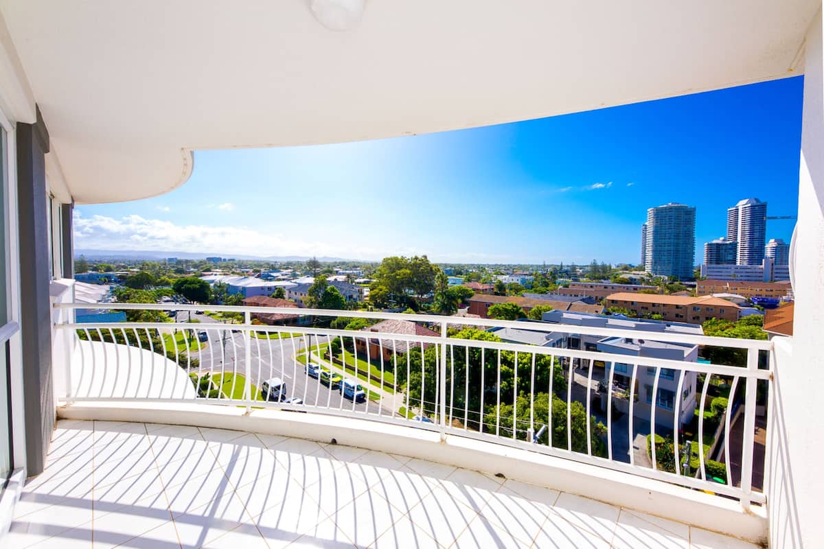 A balcony with a view of a cityscape, including buildings and greenery.