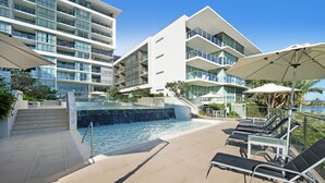 A modern hotel with a pool area, sun loungers, and a view of the ocean.