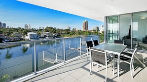 A modern balcony with a glass railing overlooking a marina and city skyline.