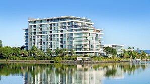 A multi-story hotel with balconies, a waterfront view, and lush greenery.