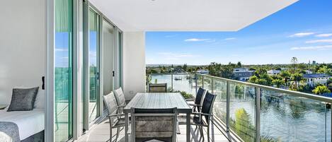 Een balkon met glazen hekwerk, met uitzicht op een wateroppervlak en een stadsgezicht.