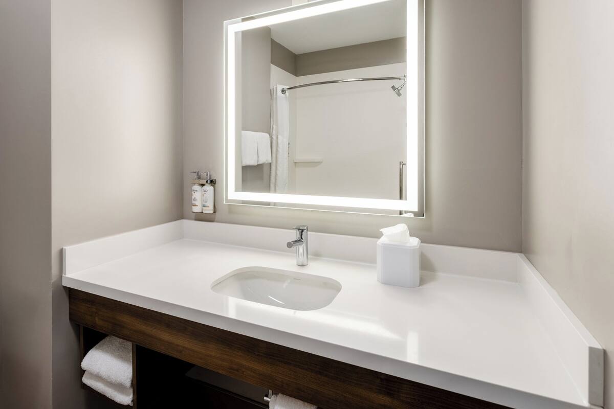 A modern bathroom with a white sink, a mirror with integrated lighting, and a wooden vanity.