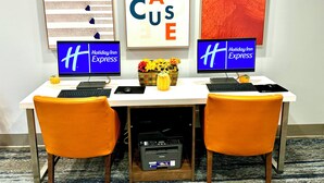 A hotel reception desk with two monitors displaying 'Holiday Inn Express' branding, a decorative wall with abstract art, and a printer. - Holiday Inn Express & Suites Dewitt (Syracuse) by IHG (East Syracuse)