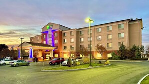 A Holiday Inn Express hotel with a parking lot, multiple cars, and a well-lit entrance. - Holiday Inn Express & Suites Dewitt (Syracuse) by IHG (East Syracuse)