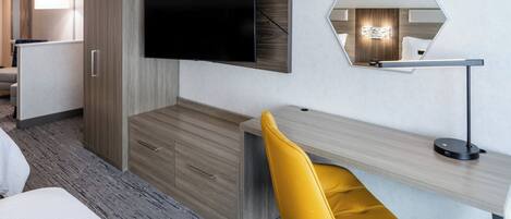Habitación de hotel moderna con una cama grande, un escritorio con silla, un televisor montado en la pared y un espejo.