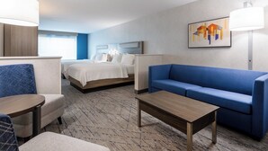 A hotel room with a bed, a blue sofa, a wooden coffee table, and a lamp. - Holiday Inn Express & Suites Dewitt (Syracuse) by IHG (East Syracuse)