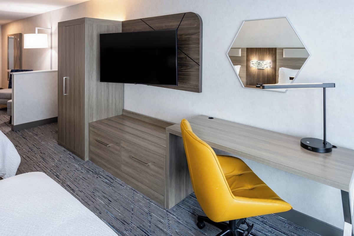 A modern hotel room with a large bed, a desk with a chair, a TV mounted on the wall, and a mirror.