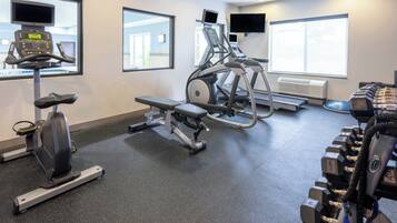 Un gimnasio con máquinas de cardio, bancos de pesas y mancuernas.