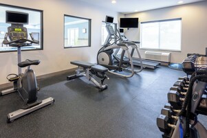 Un gimnasio con máquinas de cardio, bancos de pesas y mancuernas.