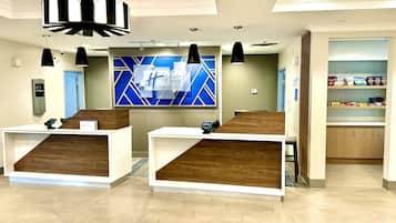 Welcome to our reception area, featuring two desks with phones and digital displays, a large wall art piece, and a convenient shelf for essentials.