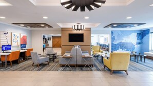 A modern hotel lobby with a seating area, a flat-screen TV, and a large abstract wall mural. - Holiday Inn Express & Suites Dewitt (Syracuse) by IHG (East Syracuse)