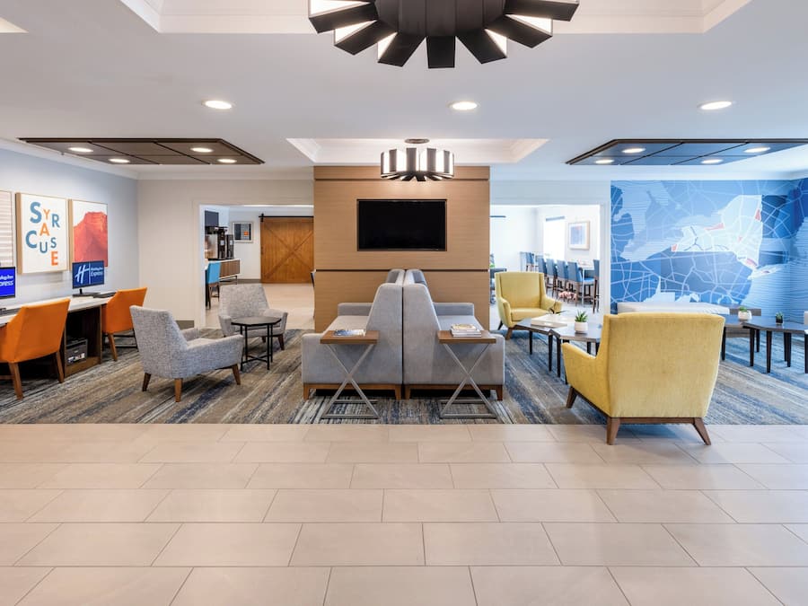 A modern hotel lobby with a seating area, a flat-screen TV, and a large abstract wall mural.