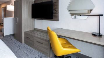 A modern hotel room with a wooden desk, a yellow chair, a flat-screen TV, and a large mirror.