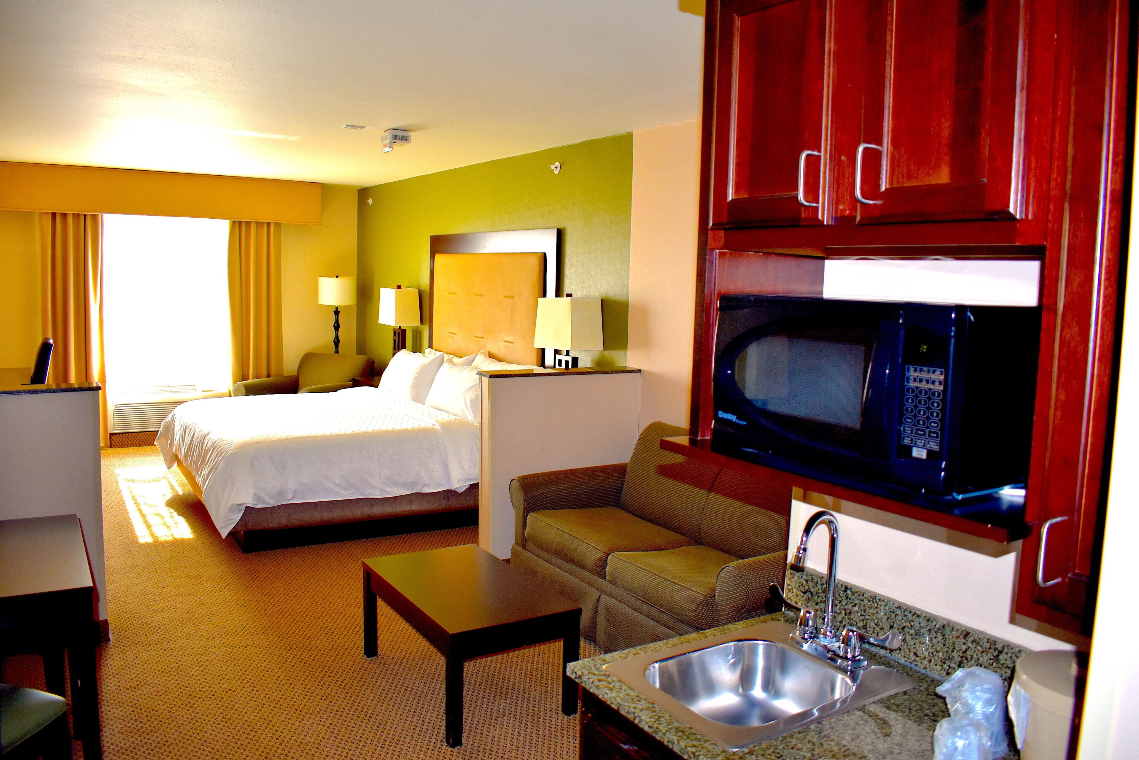 A hotel room with a bed, a sofa, a desk, a microwave, and a sink.