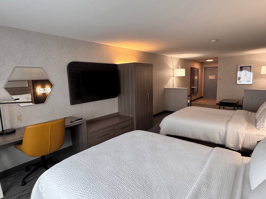 A hotel room with two beds, a desk, a chair, a TV, and a mirror.