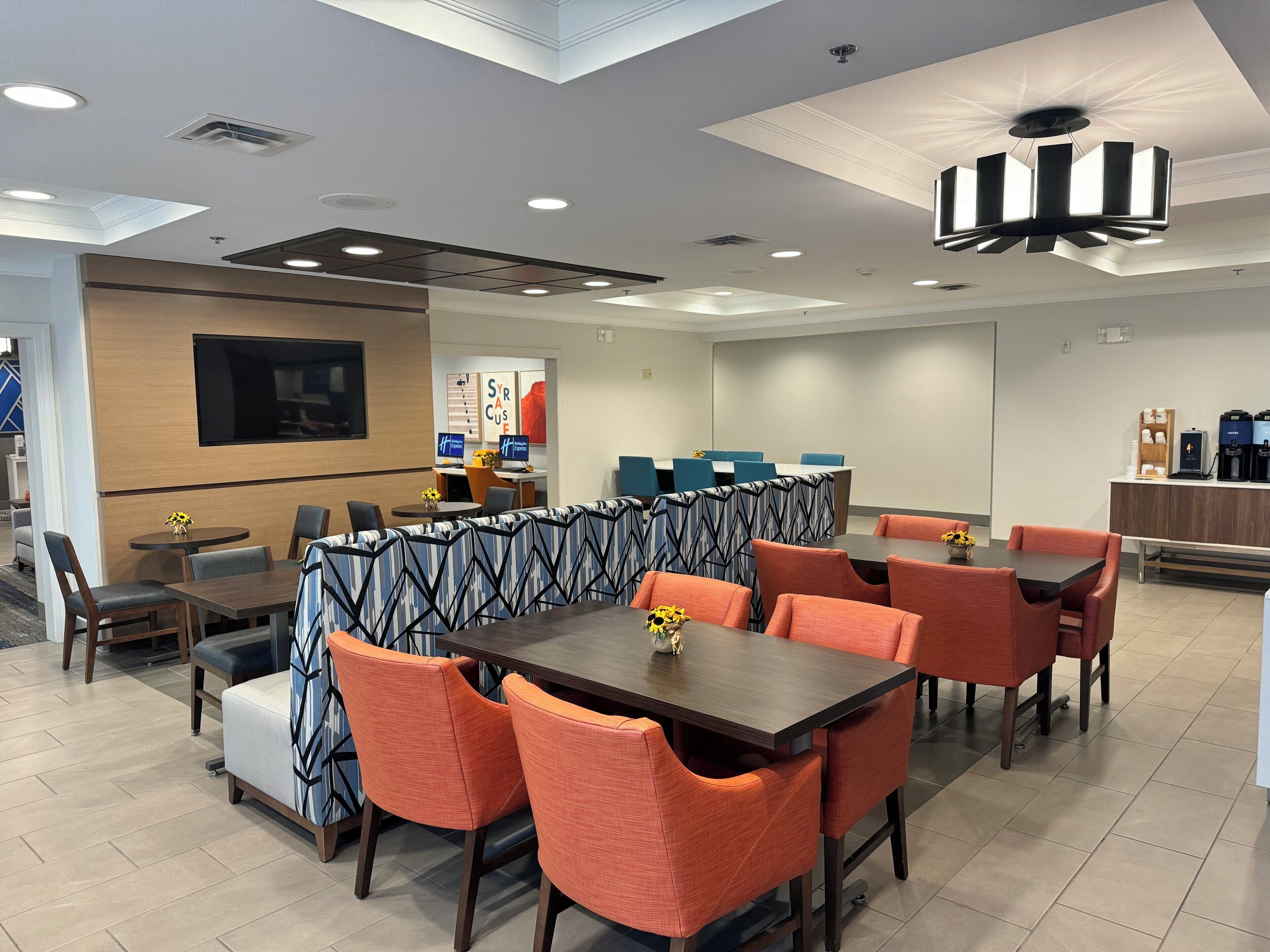 A modern dining area with high tables and chairs, a flat-screen TV, and a coffee station.