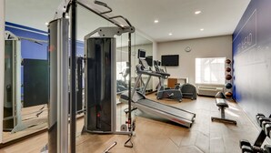 A gym with cardio machines, weightlifting equipment, and a mirrored wall.
