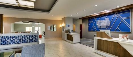 A spacious lobby with a reception desk, a blue patterned sofa, and a seating area with a table and chairs.