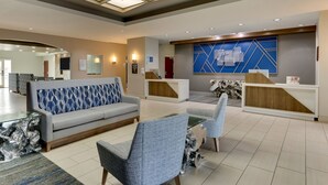 A modern hotel lobby with a grey sofa, blue patterned cushions, and a reception desk with a blue geometric wall design.