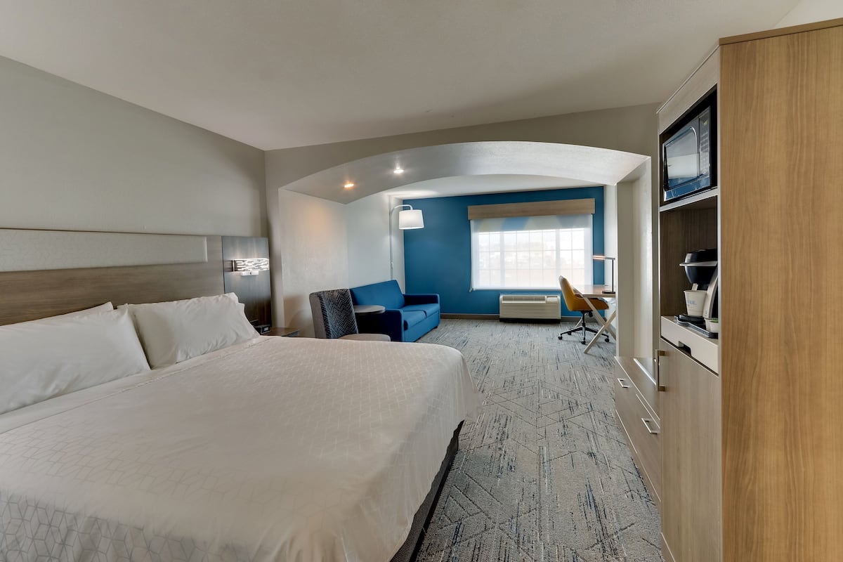 A hotel room with a large bed, a desk with a chair, a blue sofa, and a microwave.
