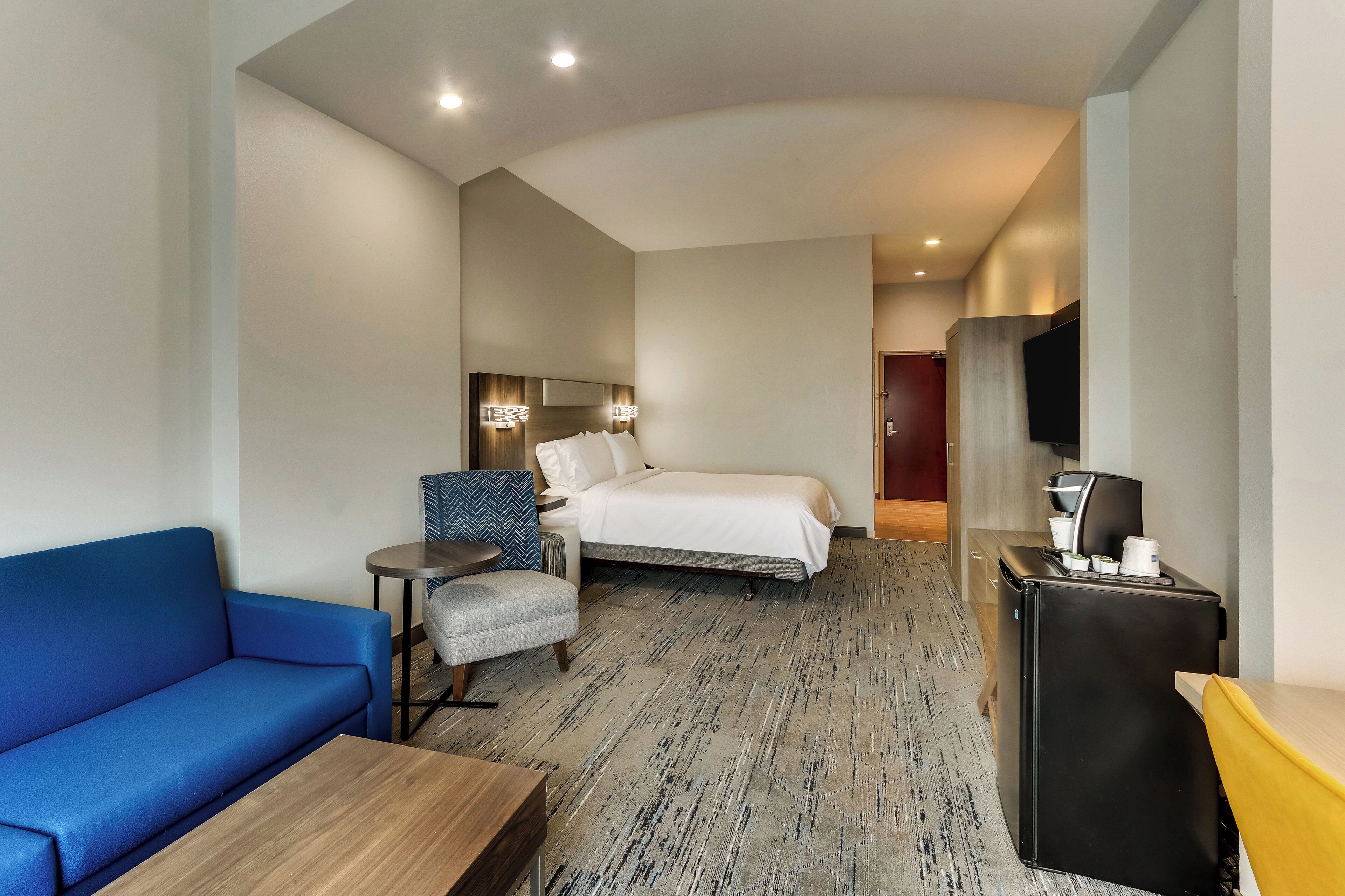 A hotel room with a bed, a blue sofa, a small table, a chair, a television, and a coffee machine.