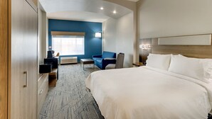 A hotel room with a large bed, a blue sofa, a small table, and a desk with a computer.