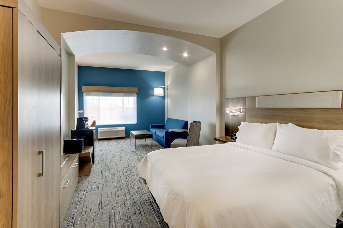 A hotel room with a large bed, a blue sofa, a small table, and a desk with a computer.