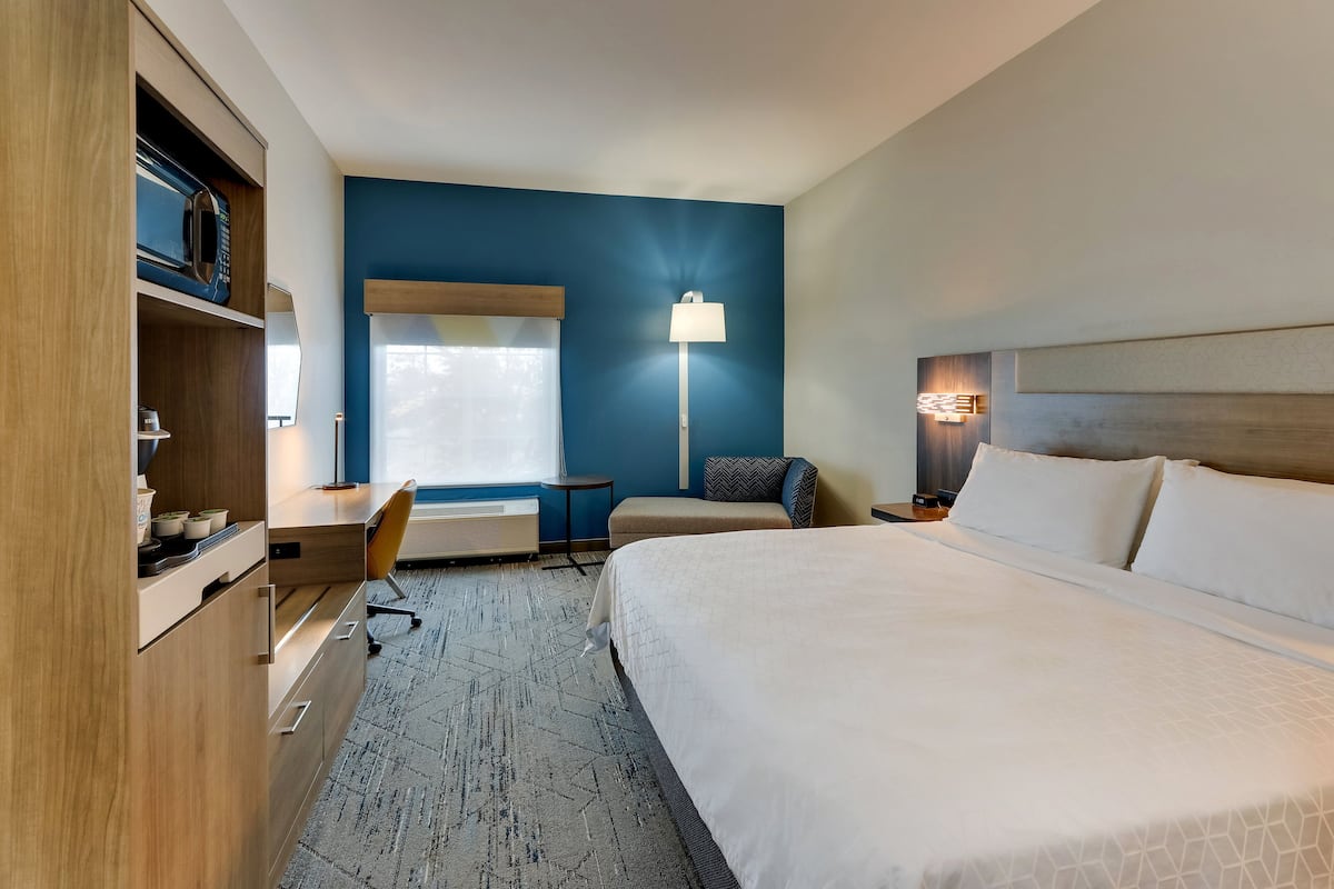 A hotel room with a bed, a desk, a chair, a lamp, and a wardrobe.
